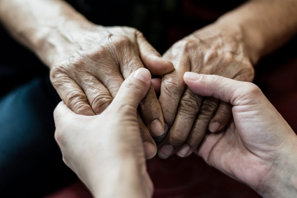 Close up of hands holding each other, one pair are visibly older with visible wrinkles while the other pair appear younger.